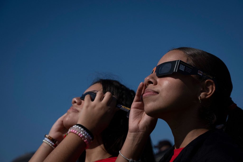 Two girls observe with special glasses the sky to watch the annular solar eclipse in Old San Juan, Puerto Rico on October 14, 2023