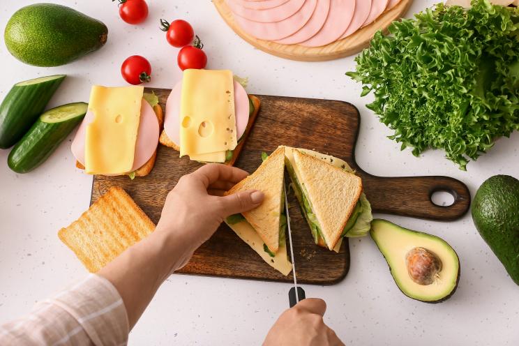 Woman cutting a tasty sandwich on a light background