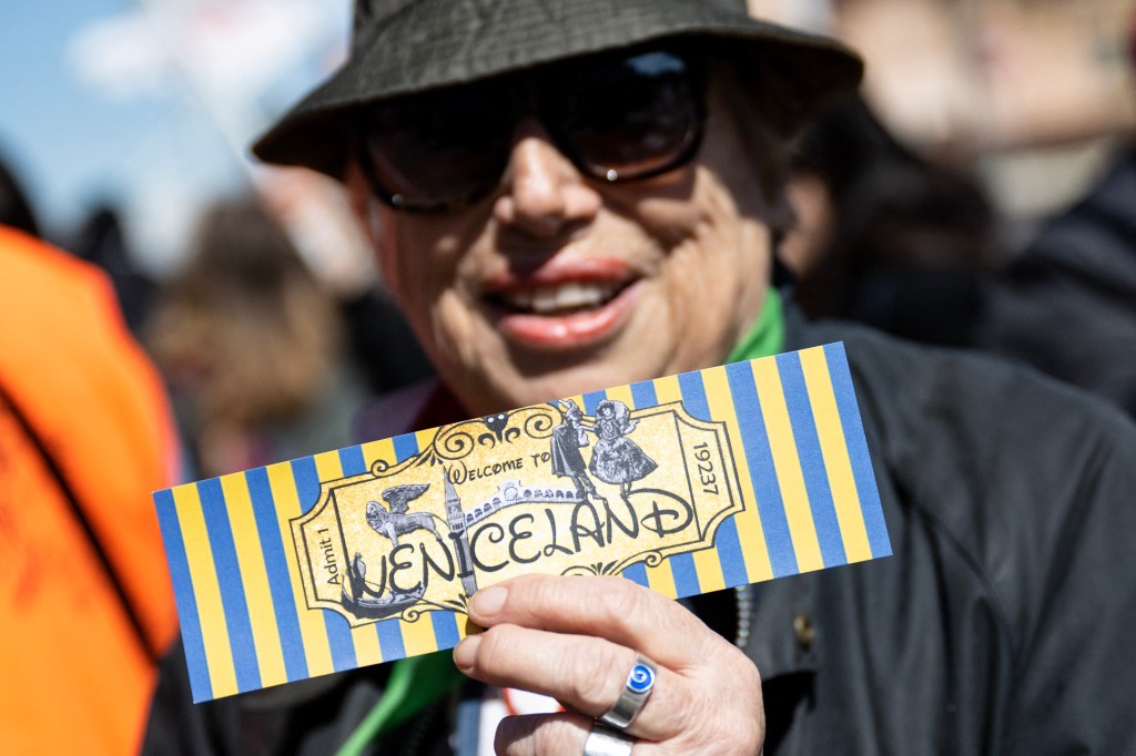 Woman protesting against 'Venice Access Fee', holding a fake ticket that reads 'Welcome to Veniceland' at Piazzale Roma, Venice.