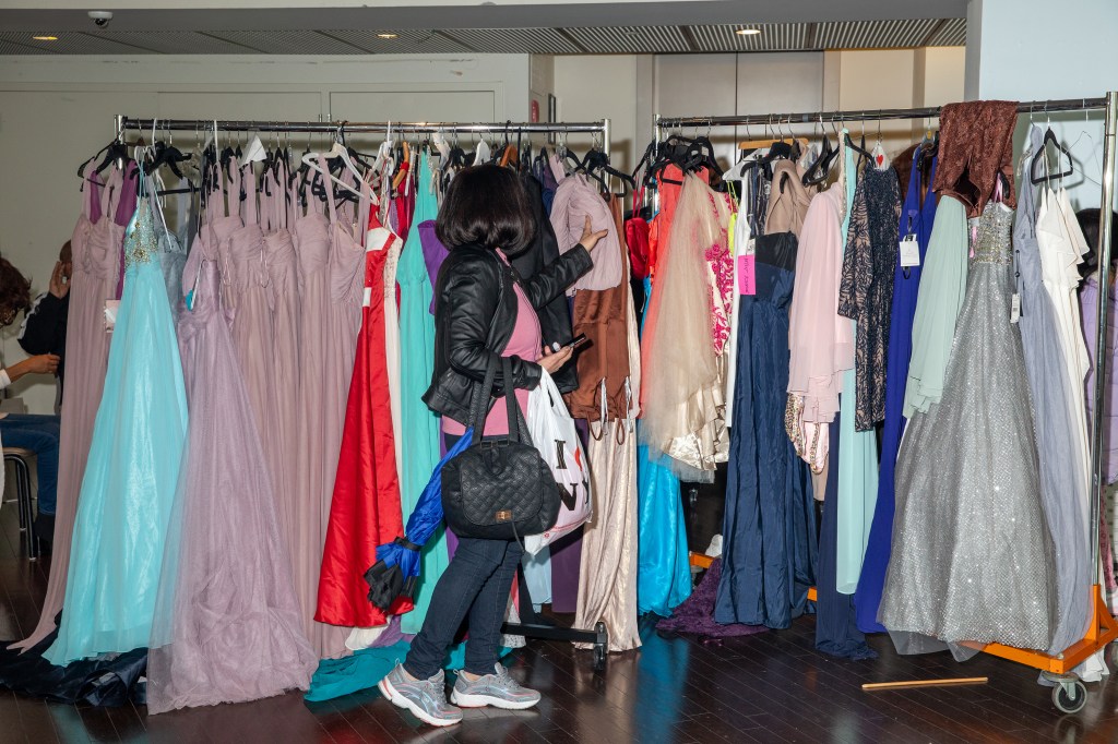 Woman browsing through brightly colored racks of dresses at a prom clothing giveaway event by Operation Prom at the Dominican Community Center, New York.