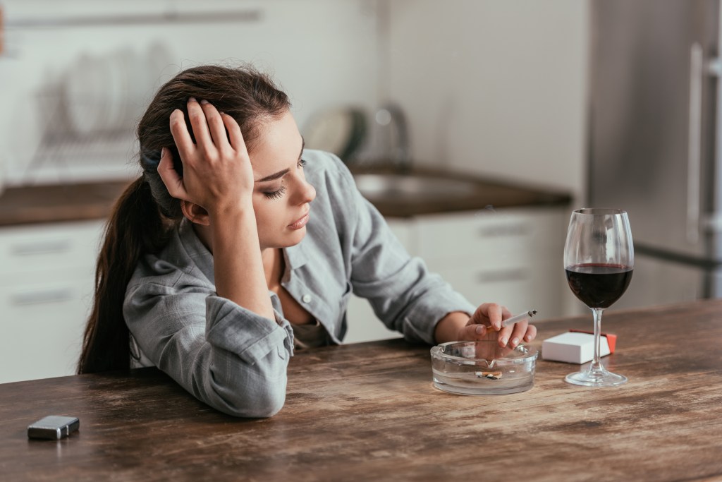 Woman sitting at a table with cigarette and wine. 