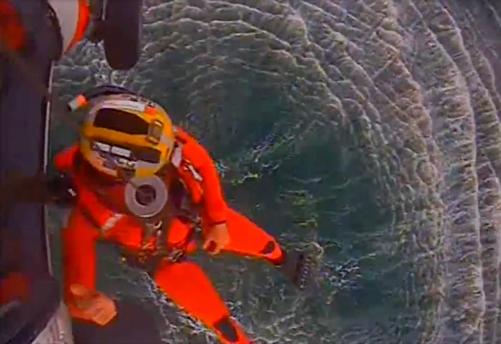 A Coast Guard rescue swimmer being lowered from a helicopter that responded to the scene.