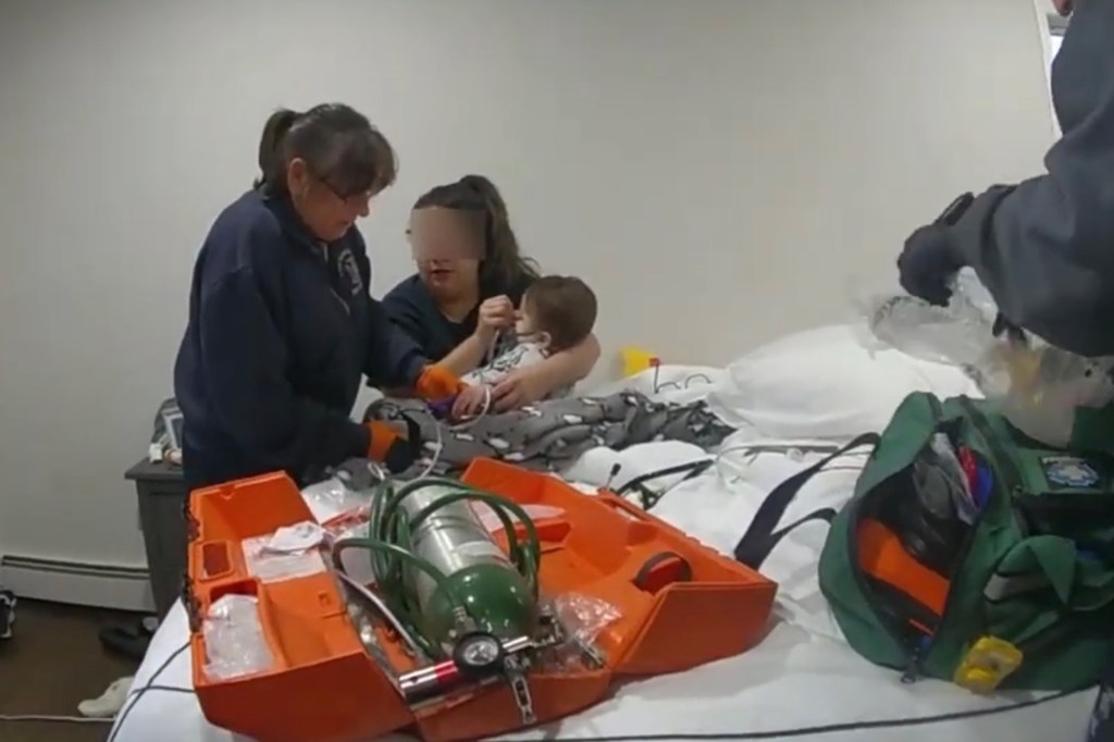 Mom holds baby as medics give him oxygen in a bedroom.