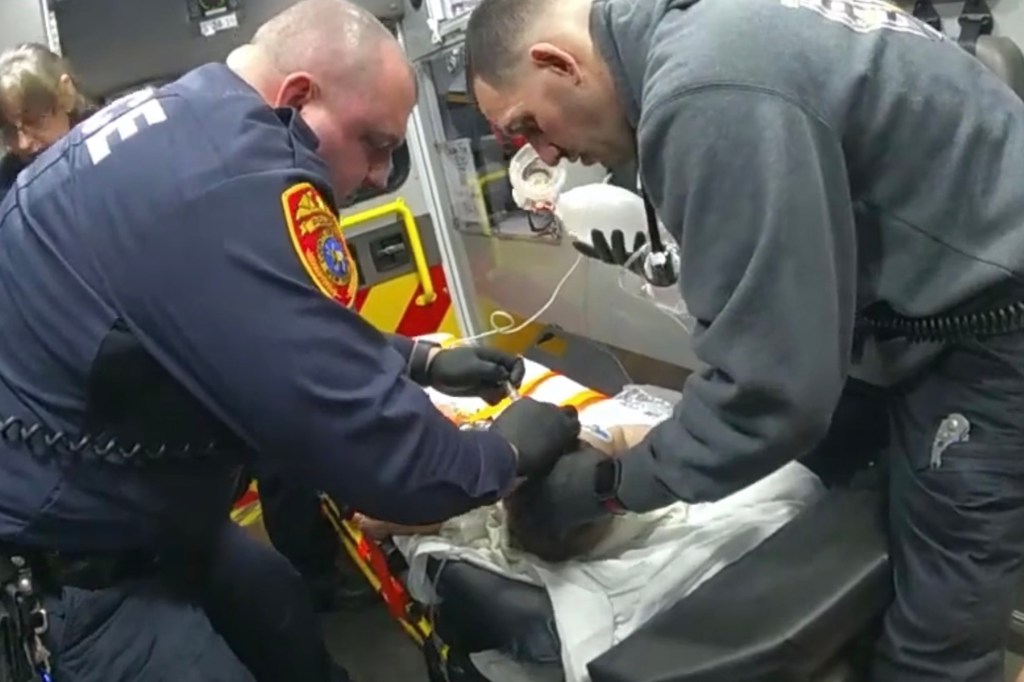 Medic administers Narcan in nose of baby on stretcher in back of ambulance. 