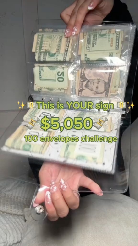 A woman holding a plastic binder full of money, representing the 100 envelope challenge on TikTok for saving money