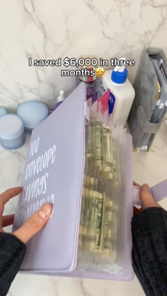 A woman holding a binder full of cash, representing successful completion of the 100-envelope saving challenge on TikTok