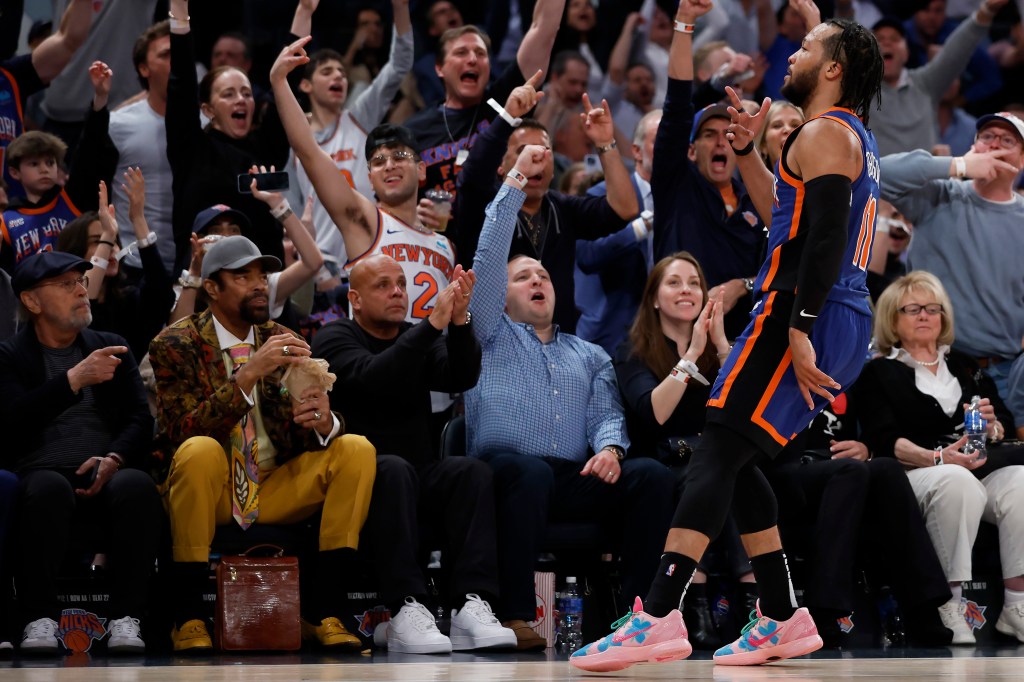 Jalen Brunson of the New York Knicks celebrating after a three-point basket during a playoff game against the Indiana Pacers, with Walt Frazier and crowd in the background