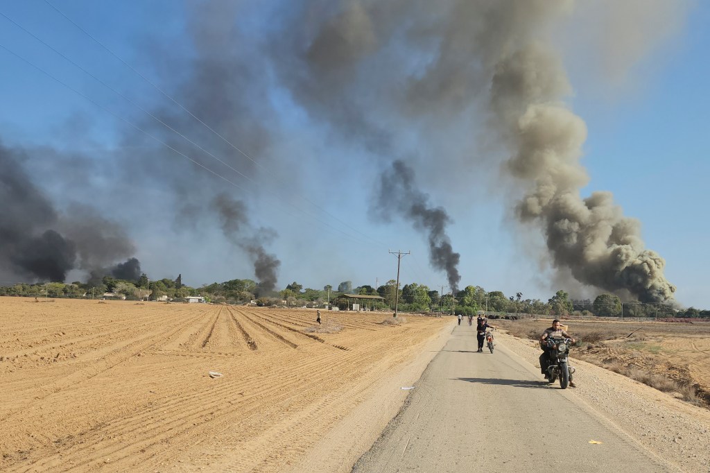 Palestinians walking away from Kfar Azza, Israel with a backdrop of black smoke, near the fence with the Gaza strip following a multi-front attack by Hamas on October 7, 2023