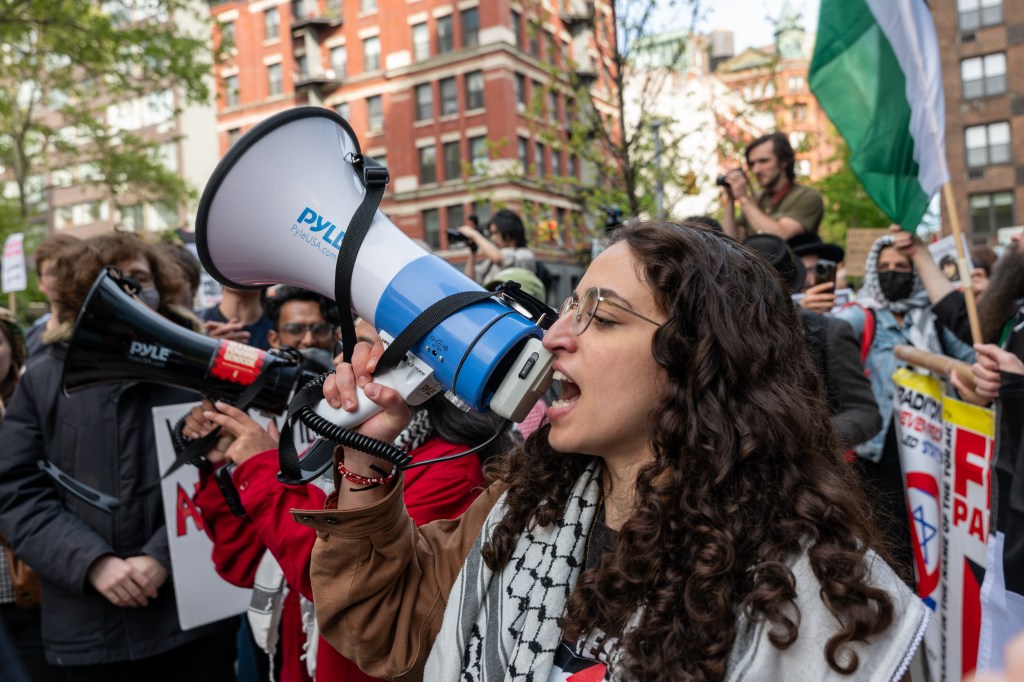 Pro Palestinian protesters demonstrating outside New York University buildings, with a woman speaking into a megaphone, May 2024