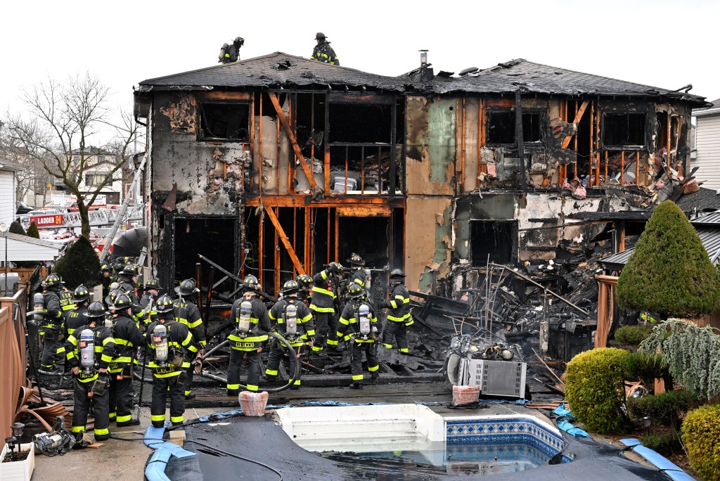 Firefighters standing outside a severely burned, two-story wooden house on Staten Island, taken on February 17, 2023 following a fire incident that left three firemen critically injured
