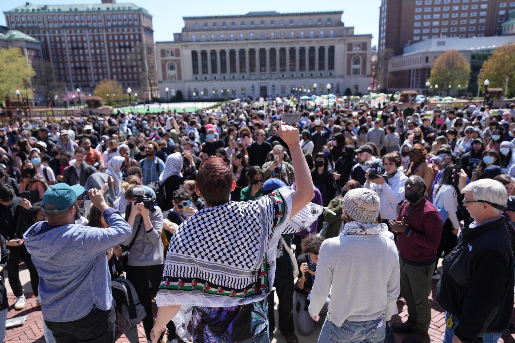 A man in a keffiyeh speaks to a large crowd at Columbia