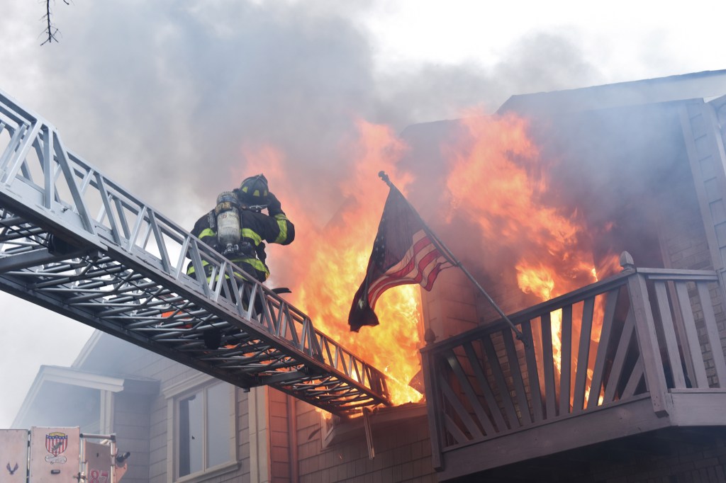 Firefighter on a ladder at the scene of a 5th alarm fire in Staten Island, with the house partially collapsed and two firefighters injured