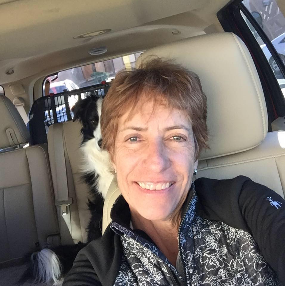 Kim Lark in the driver's seat of a car, with a dog sitting behind her