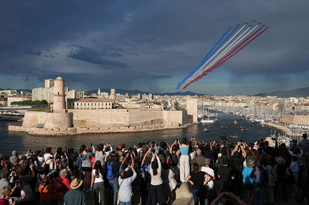 The Patrouille de France aerobatics demonstration aircraft leave a tricolor trail of smoke in the sky as the Belem, the three-masted sailing ship bringing the Olympic flame from Greece, enters the Old Port in Marseille, southern France, Wednesday, May 8, 2024.