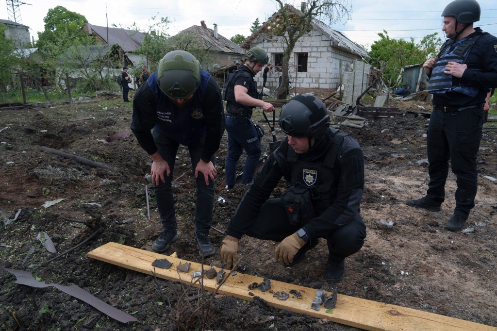 A Ukrainian police officer and war crime prosecutor inspect fragments of a glide bomb