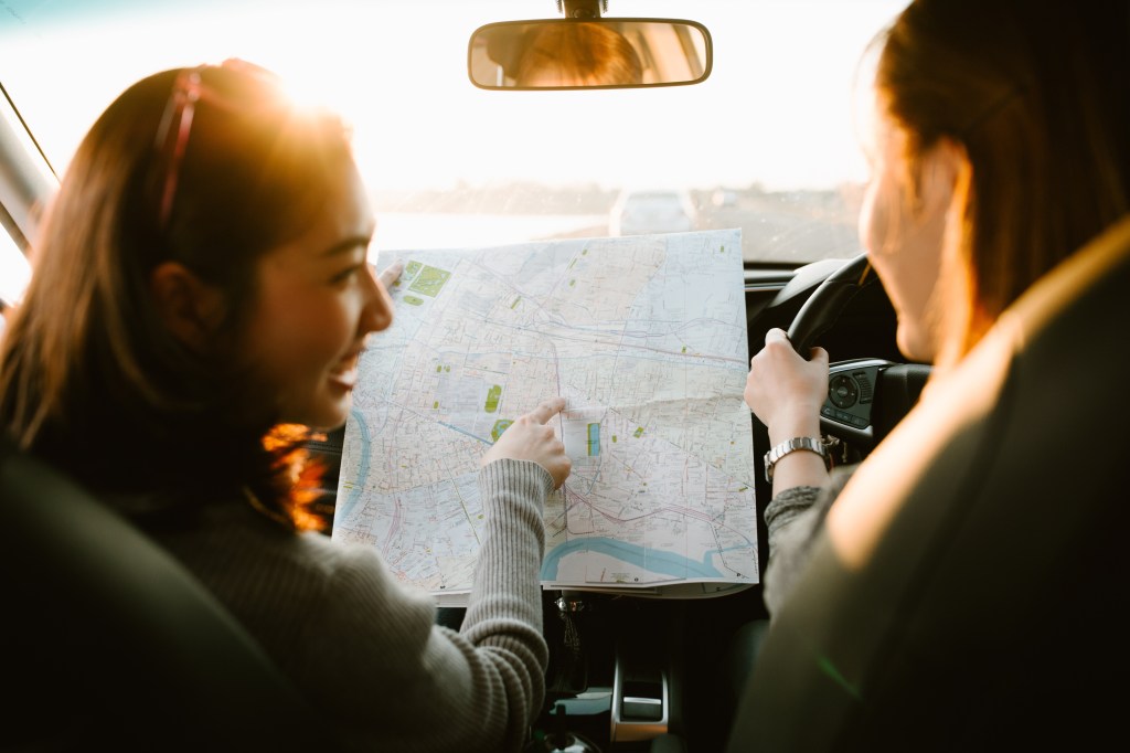 Lost with map two young Asia woman friends in car enjoy road tri