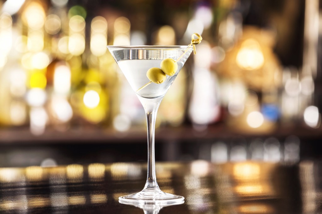 Closeup glass of martini dry cocktail with olives at bar counter background.