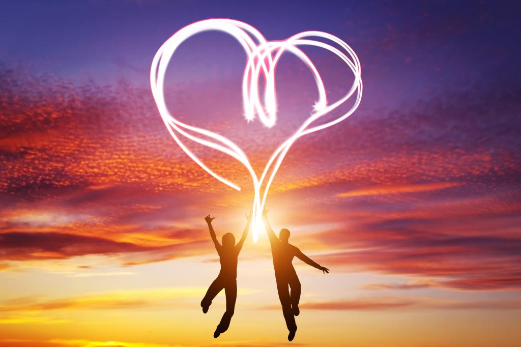 Happy couple jump together and make a heart symbol of light manifesting their love. Romantic sunset sky, Valentines Day.