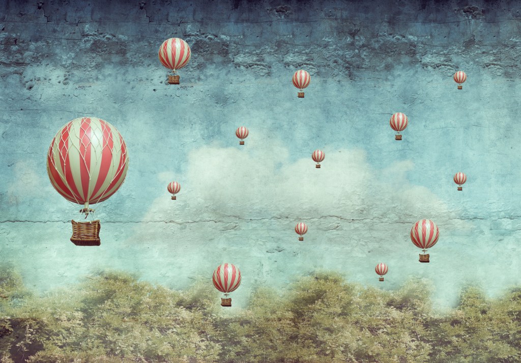 Many hot air balloons flying over a forest