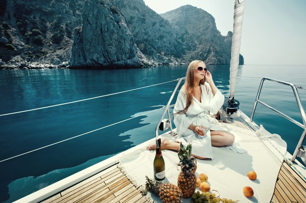Luxury vacation at sea on yacht. Beautiful woman with wine, fruit and mobile phone on boat