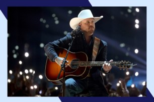 Cody Johnson strums the guitar onstage while wearing a cowboy hat.