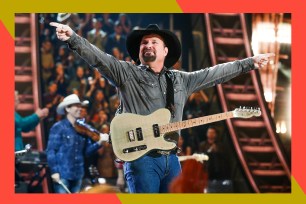 With a guitar slung over his shoulder, Garth Brooks smiles and points to the crowd.