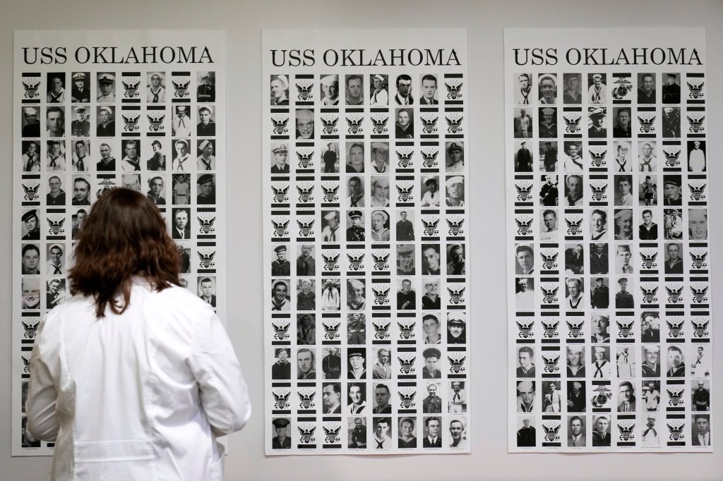 Defense POW/MIA Accounting Agency forensic anthropologist Carrie Brown looks at photos of service members from the USS Oklahoma on a wall at Offutt Air Force Base, Monday, May 20, 2024, in Bellevue, Neb. 