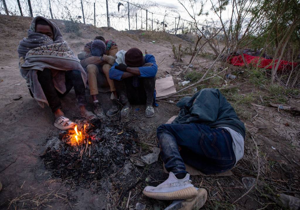 African migrants sleep next to a fire in order to keep warm in the early hours of the morning on the Rio Grande in El Paso, Texas on March 21, 2024.