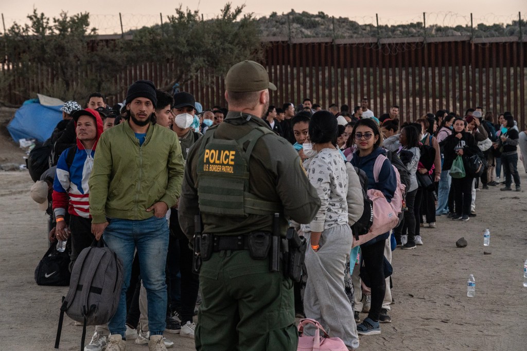 Asylum-seeking migrants for a line as they wait to be transported by U.S. Border Patrol agents after crossing the border into the U.S. from Mexico in Jacumba Hotsprings, California on November 6, 2023
