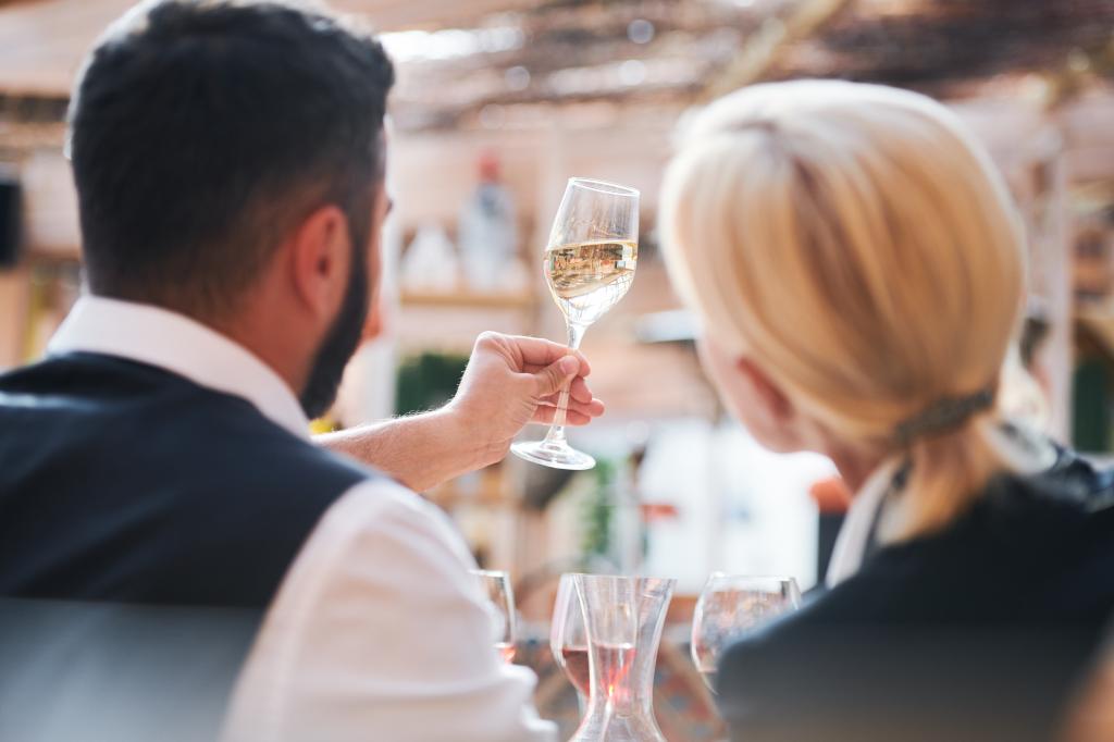 Back view of a man and woman, professional cavists, analyzing a sample of wine in a flute glass