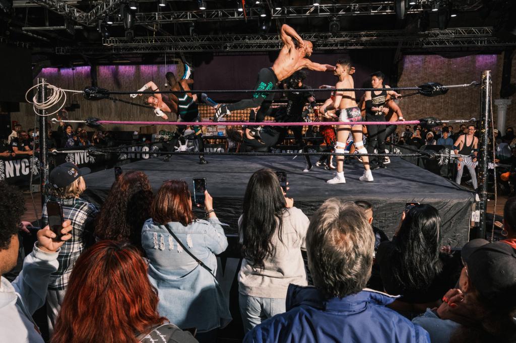 Fans watch and record on iPhones as several wrestlers fight in the ring at House of Glory. 