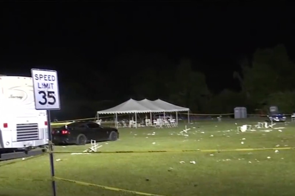 A car parked in a field next to a white tent and a sign, at the site of the May day event in Stockton where shootings occurred.