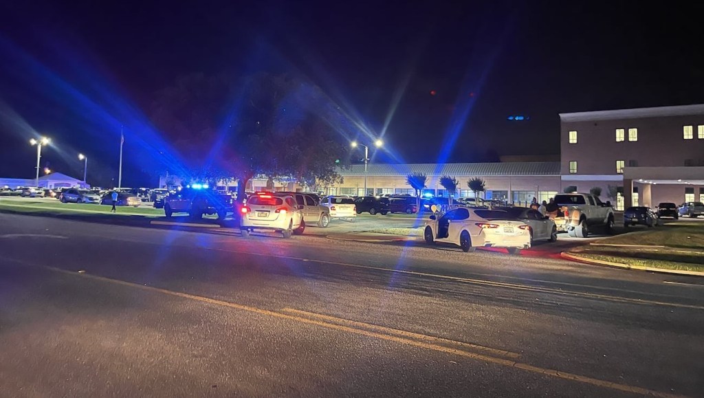 Police cars parked on the side of a road with flashing blue lights during an investigation of a mass shooting event