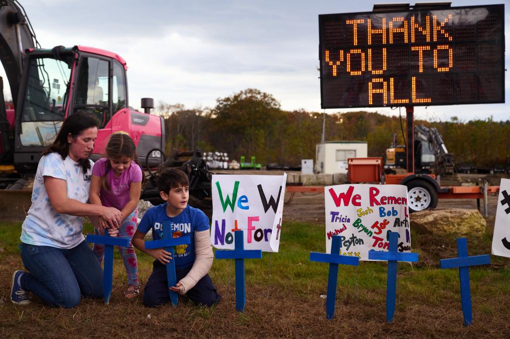 Bre Allard, and her children Lucy, 5, and Zeke, 8, plant crosses and signs near the Schemengees Bar & Grille after 18 victims were killed in a mass shooting on Saturday, October 28, 2023 in Lewiston, Maine.