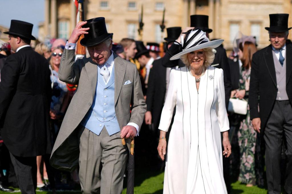 King Charles III and Queen Camilla walking down a lawn at a Royal Garden Party at Buckingham Palace