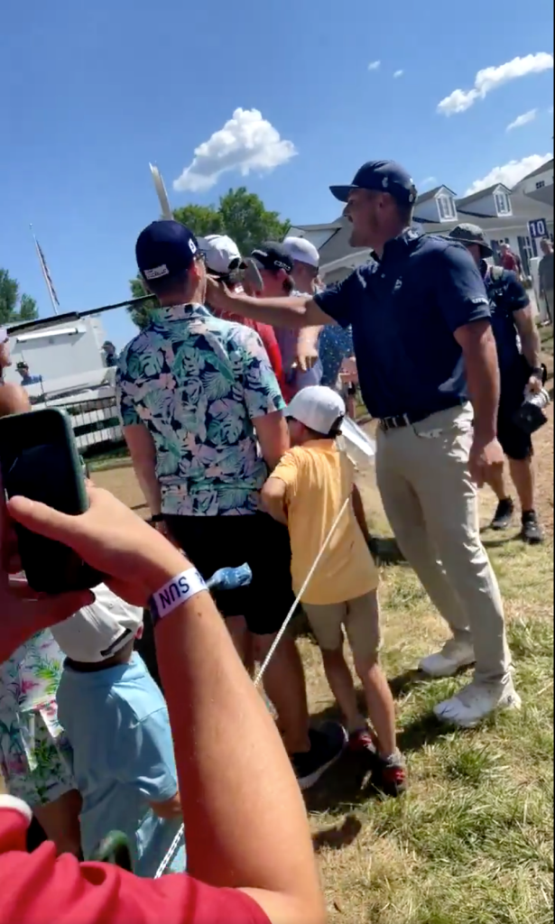 Bryson DeChambeau points his golf club at the adult who was running off with a golf ball. 