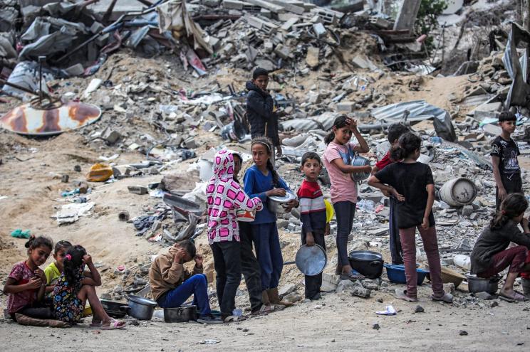 Children wait with pots to receive food rations from an outdoor kitchen in Khan Yunis in the southern Gaza Strip