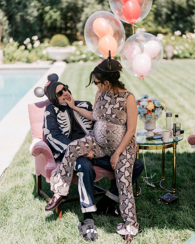 Travis Barker, positive for COVID, sitting and getting affectionate with a pregnant Kourtney Kardashian at a Disney-themed baby shower
