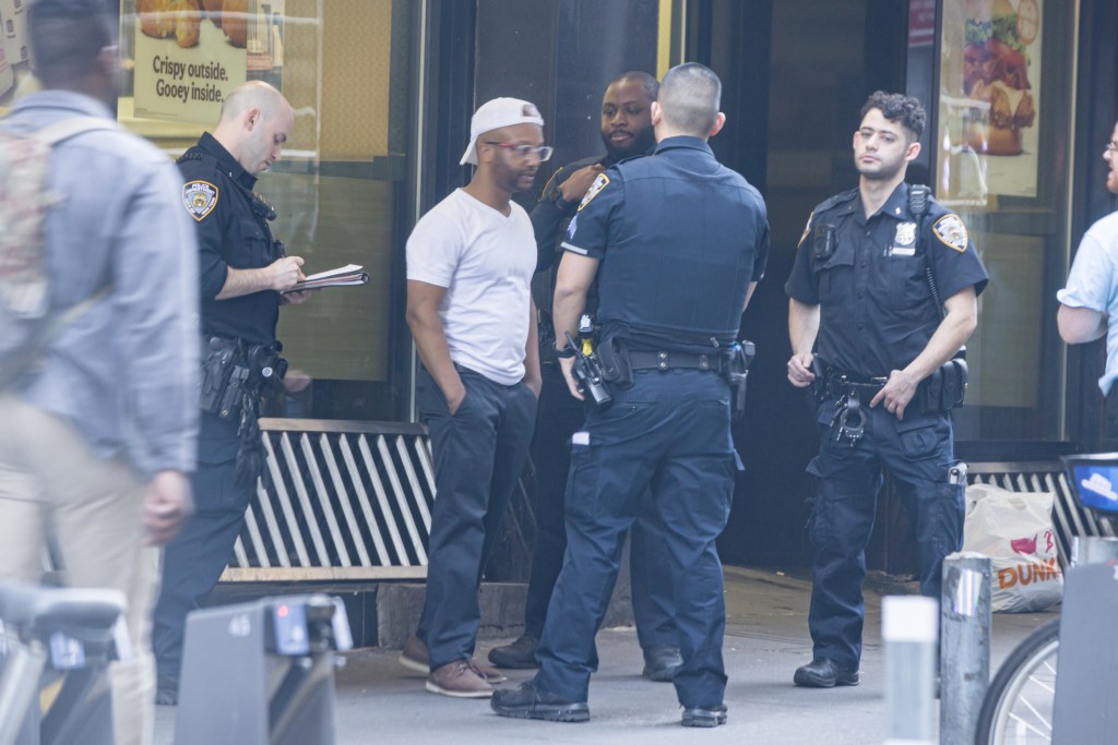 a man in a white shirt dark jeans and a white backwards baseball cap speaking to police officers outside the burger king