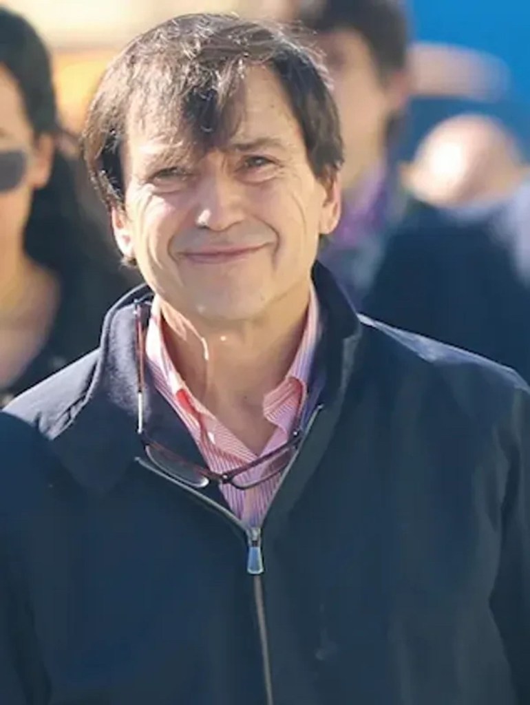 Brad Zackson outside in the sun, looking at the camera wearing a pink top and navy blue zippered sweater