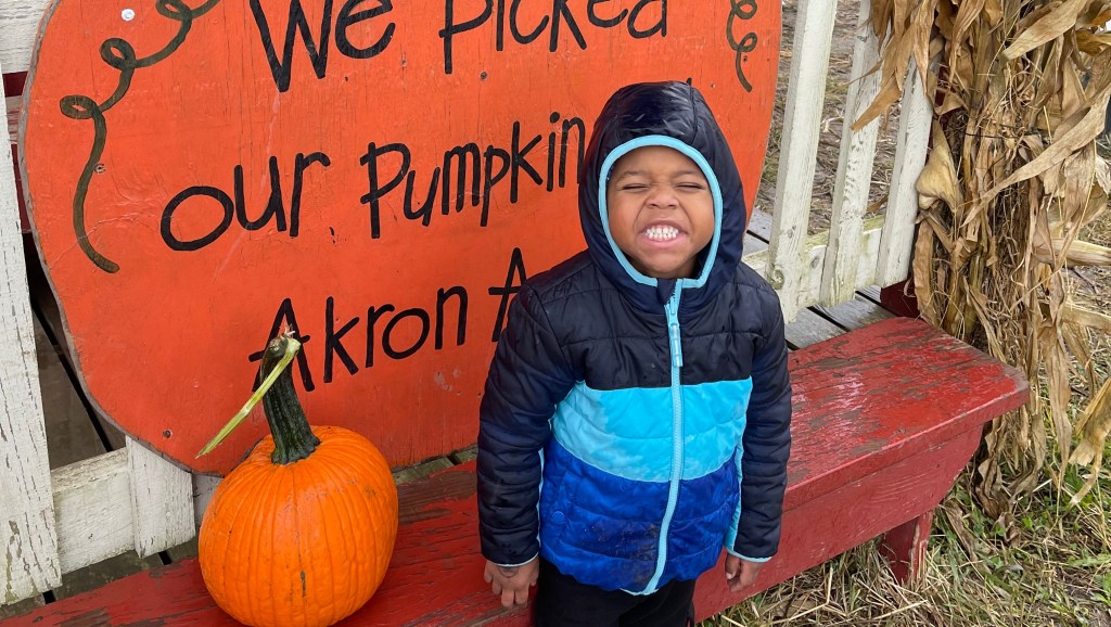 Five-year-old boy, Ezra Toczek, standing in front of a pumpkin