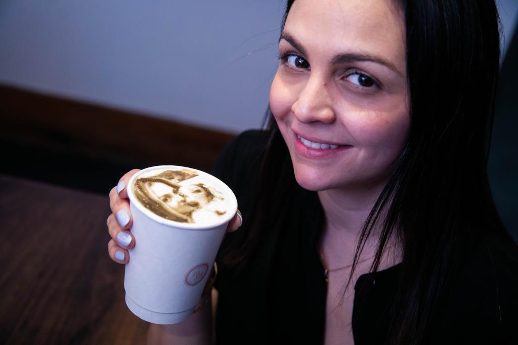 Moka Matcha Cafe's social media manager Gabriela Rodriguez, looking at the camera and smiling while holding a latte she made for The Post with a photo on the foam using a photo of her and her pup, Sheldon. 