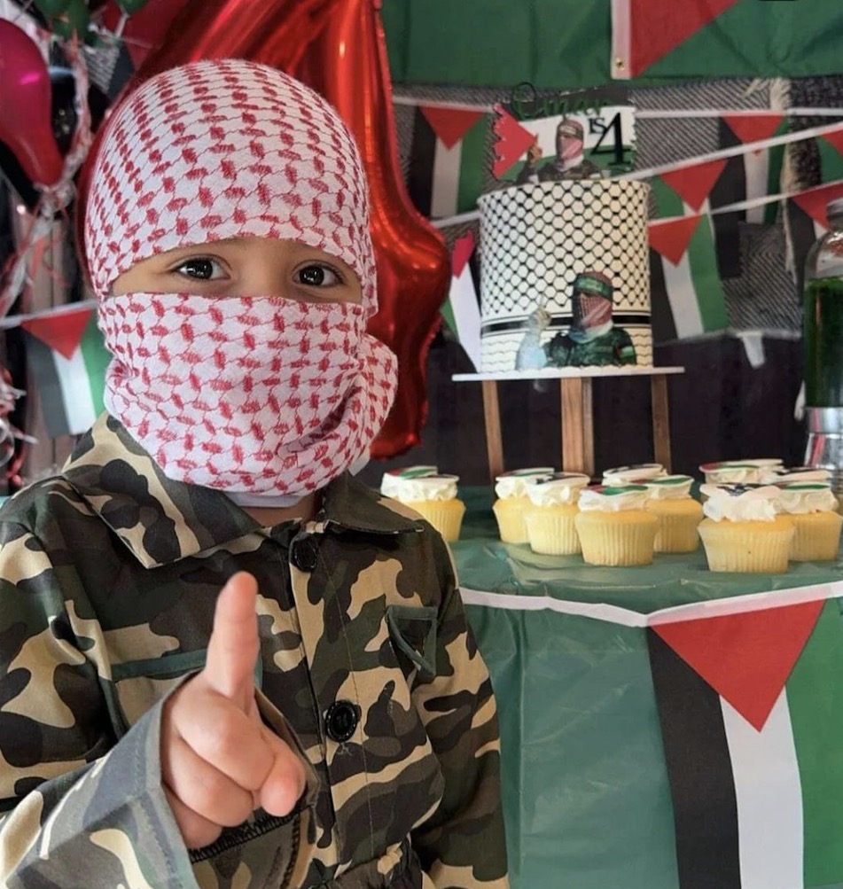 Four-year-old boy standing next to a large birthday cake decorated with the Palestinian flag and a picture of a notorious figure, in a Sydney bakery