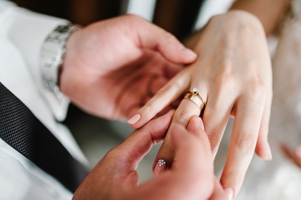 The hands of the groom wears a wedding engagement ring on the finger of the bride. 