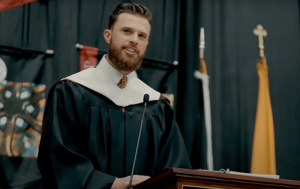 Harrison Butker delivering Commencement Address in a graduation gown at Benedictine College in 2024