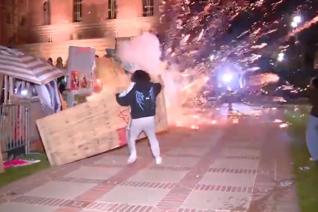 Person in riot gear amid a scene of unrest at a pro-Palestine encampment at UCLA, with fights and firecrackers being thrown