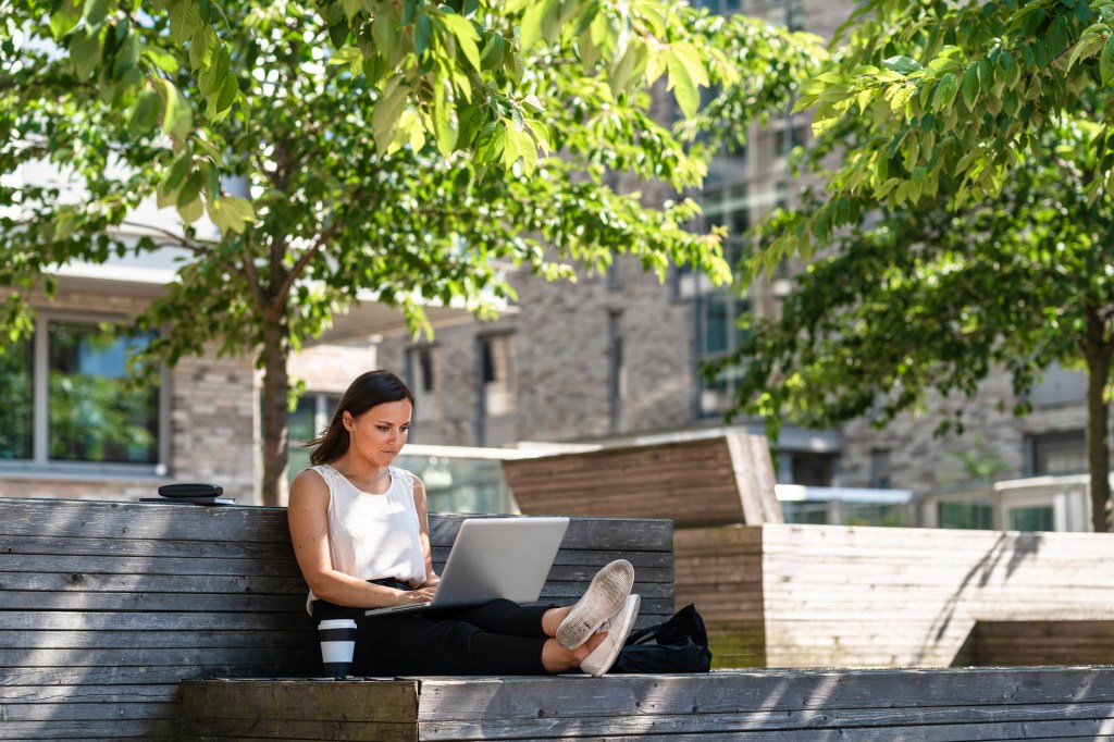 A freelance woman working on her laptop and smartphone while sitting on a bench
