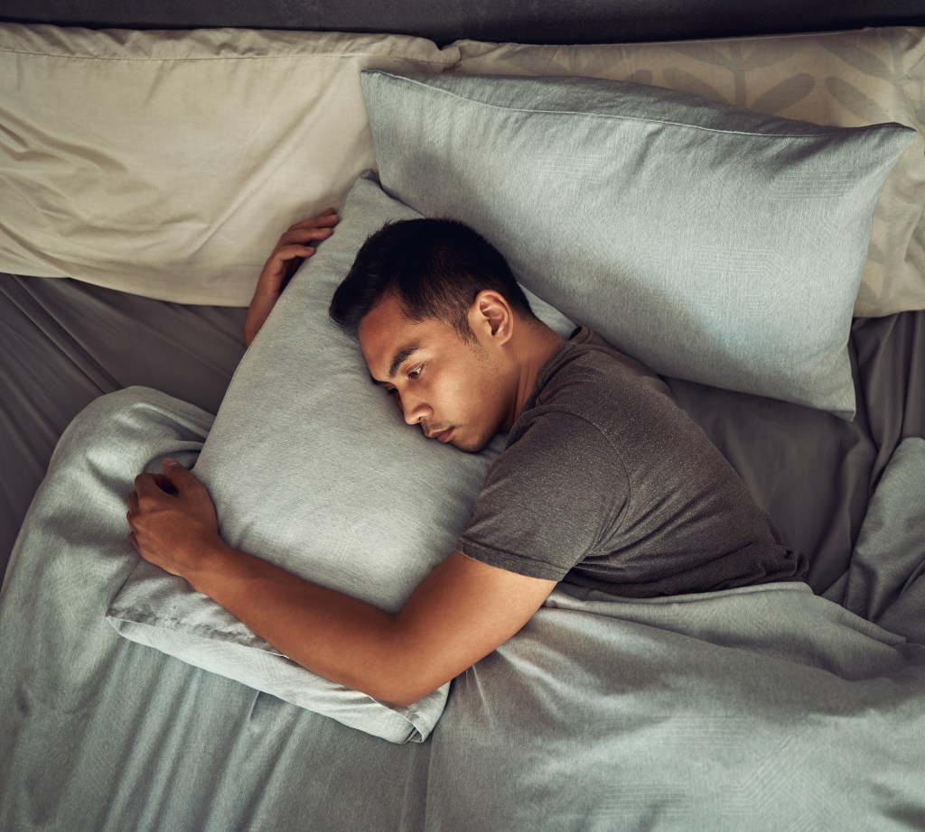 Shot of a young man lying in bed and looking unhappy at home.