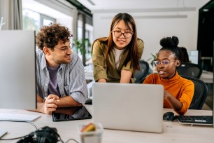 Three young colleagues discussing work at a modern office, looking at a laptop