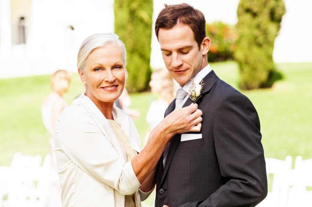 Portrait of happy mother pinning corsage on groom's suit at outdoor wedding. 